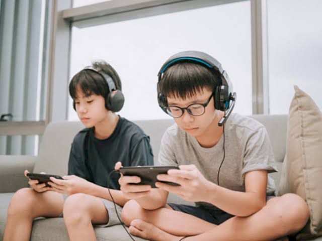 Seorang remaja duduk terpaku di depan layar komputer di kamar gelap, menggambarkan efek bermain game online berlebihan pada pola tidur